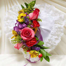 Bright pink and red floral spray with yellow accents on a white lace heart pillow and purple ribbon.