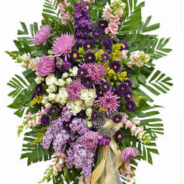 Tall standing spray of purple, pink, and white flowers with large green leaves on an easel