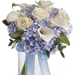 White roses and calla lilies in a glass vase with pale blue ribbon