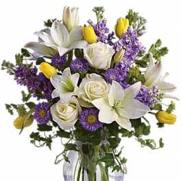 White lilies, roses, and purple flowers in a clear glass vase