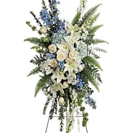 Standing floral spray with white lilies, cream roses, and blue flowers