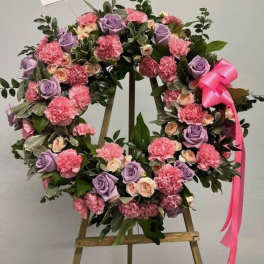 Standing wreath of pink carnations and lavender roses with a pink bow on a wooden easel