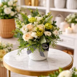 Cream and pale yellow roses in a white dotted pot with a striped ribbon.