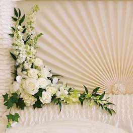 Corner arrangement of white roses and other white flowers with trailing greenery on a textured cream backdrop