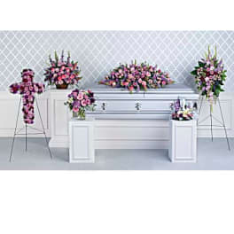 Floral funeral display with pink and purple arrangements around a white casket