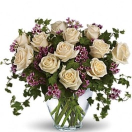 Cream roses in a clear glass vase with purple filler flowers