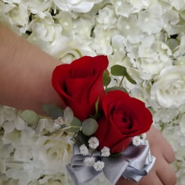 Red rose wrist corsage with silver ribbon on a hand against white flower backdrop