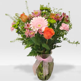 Mixed bouquet of pink gerbera, orange roses, and green button mums in a glass vase with pink ribbon.