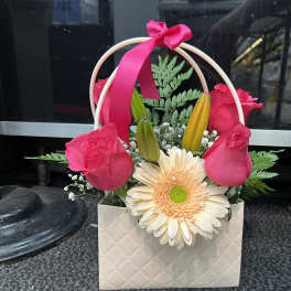 Pink roses and a cream gerbera daisy in a gift bag with a ribbon handle