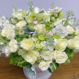 White and pale green floral arrangement in a round box