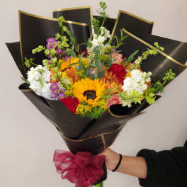 Mixed bouquet with a sunflower, roses, and white blooms wrapped in black paper
