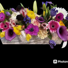 Mixed bouquet with purple, pink, yellow, and white flowers in a wooden container
