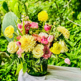 Mixed yellow and pink flower arrangement in a green glass vase