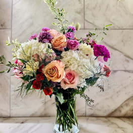 Mixed bouquet of roses, hydrangeas, and carnations in a glass vase
