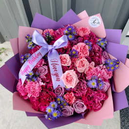 Pink and purple bouquet of roses, carnations, and small daisy-like flowers with ribbon