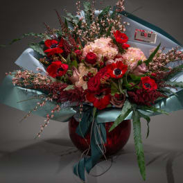 Bouquet of red and blush flowers in teal wrapping with a red vase