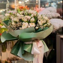 Bouquet of white flowers wrapped in green paper with a pink ribbon