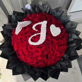 Round bouquet of red roses with white floral initials and a heart on black wrap