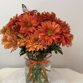 Orange chrysanthemum bouquet in a glass vase with a ribbon