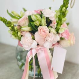 Pink and white bouquet in a glass vase with a ribbon and card