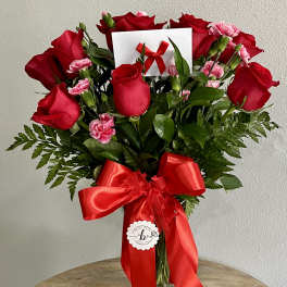 Bouquet of red roses and pink carnations in a glass vase with a red ribbon