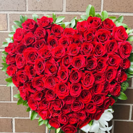 Heart-shaped arrangement of red roses with a white ribbon bow