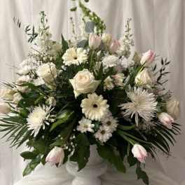 White floral arrangement in a white pedestal vase with pink tulips and roses