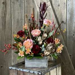 Mixed floral arrangement in a gray wooden box with burgundy and peach blooms