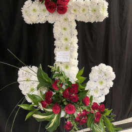 White floral cross with red roses and greenery on a black backdrop