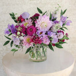 Low glass vase of pink and purple mixed flowers arranged in a lush, rounded centerpiece