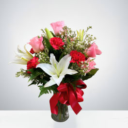 Bouquet of pink roses, white lilies, and red carnations in a glass vase with a red ribbon