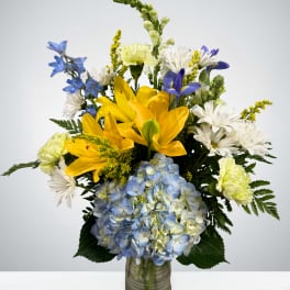 Bouquet of yellow lilies, blue hydrangea, and white daisies in a glass vase