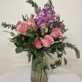 Pink roses and purple flowers arranged in a clear glass vase