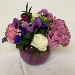 Mixed bouquet of pink, purple, and white flowers in a purple glass vase