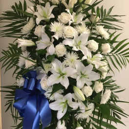 White floral standing spray with lilies, roses, and a blue ribbon