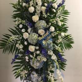 Large standing floral spray with white and blue flowers and a ribbon tribute