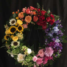 Colorful floral wreath with roses, sunflowers, and purple blooms on a black stand