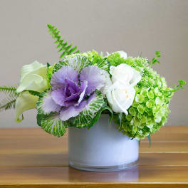 Purple and white flowers arranged in a round glass vase