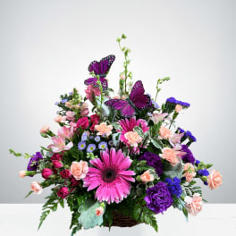 Mixed pink and purple flower arrangement in a basket with butterfly accents