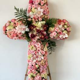 Large floral cross covered in pink roses and orchids on an easel