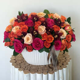 Large bouquet of pink, orange, and cream roses in a white vase