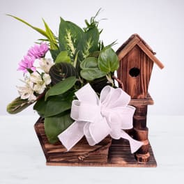 Lush green plants with pink and white flowers in a rustic wooden birdhouse planter with a white bow