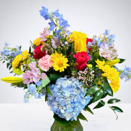Mixed bouquet in a glass vase with blue hydrangea, yellow daisies, and red roses