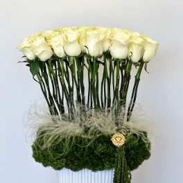 Tall arrangement of white roses in a white vase with green moss