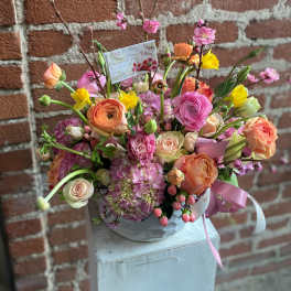 Mixed bouquet of pink, peach, and yellow flowers in a round container