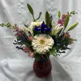 Mixed bouquet with a white gerbera daisy, lilies, and purple accents in a red vase