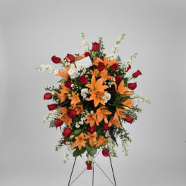 Standing floral spray with red roses and orange lilies on a metal easel