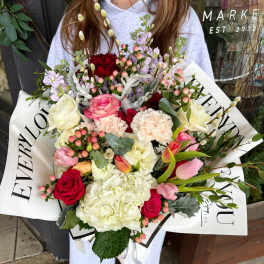 Large bouquet of mixed pink, white, and red flowers wrapped in white paper
