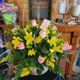 Pink roses and yellow lilies in a round basket arrangement