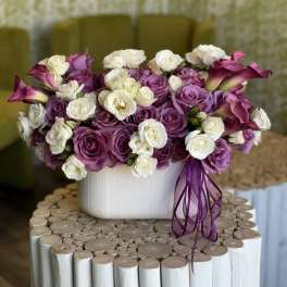 Purple and white rose arrangement in a white vase with calla lilies